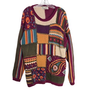 May include: A patchwork sweater with a round neckline. The sweater features a variety of colors and patterns, including floral, striped, and paisley designs. The sleeves are long and the overall style is vintage.