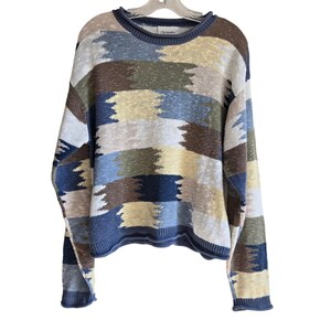 May include: A long-sleeve knit sweater featuring a horizontal block pattern in shades of blue, brown, cream, and olive green. The garment has a crew neckline with a ribbed collar, cuffs, and hem, and includes a visible brand label at the neck.