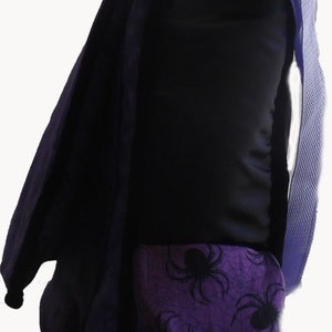 May include: Purple backpack with a black spider web and spider design on the front pocket. The backpack has a purple strap.