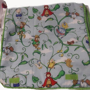 May include: A blue and green fabric tote bag with a whimsical design featuring characters climbing a beanstalk. The characters include a girl in a red hooded cloak, a girl in a blue dress, a boy in a green shirt, and a pig in a pink dress. The bag has a green and white trim.