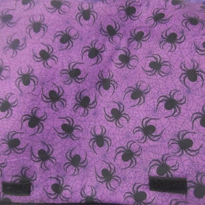 May include: Purple fabric bag with a black spider web pattern and black spiders. The bag has two black straps.