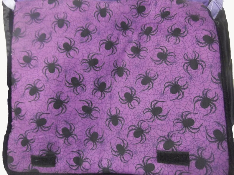 May include: Purple fabric bag with a black spider web pattern and black spiders. The bag has two black straps.