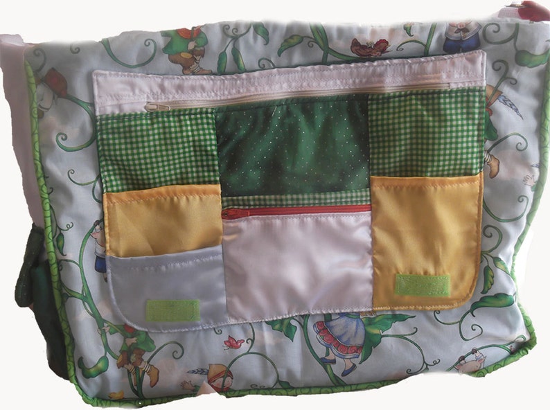 May include: A green and white patchwork fabric bag with a zippered pocket and multiple smaller pockets. The bag features a whimsical design of a girl climbing a beanstalk.