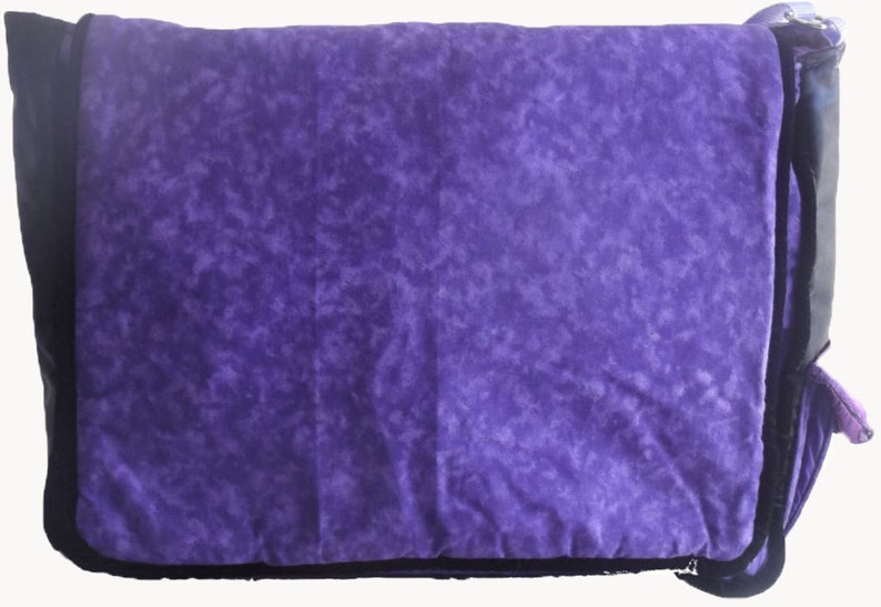 May include: Purple and black messenger bag with a tie-dye pattern. The bag has a flap closure and a zippered pocket on the front.