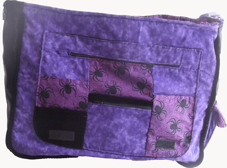 May include: Purple patchwork messenger bag with a spiderweb pattern and multiple zippered pockets.