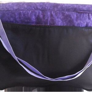 May include: Purple and black messenger bag with a long adjustable strap. The bag has a zippered closure and a front pocket.