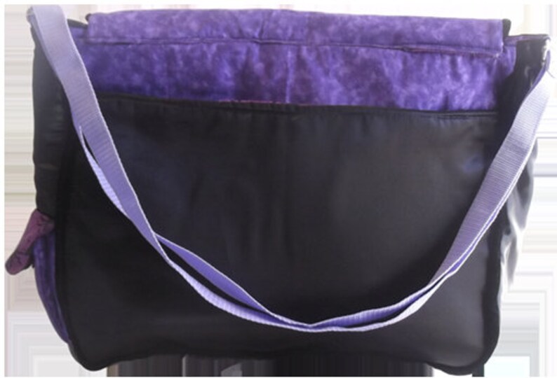 May include: Purple and black messenger bag with a long adjustable strap. The bag has a zippered closure and a front pocket.