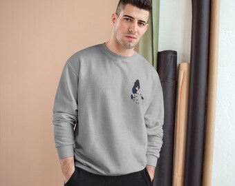 Può includere: Una felpa grigio chiaro con una piccola grafica di un personaggio anime sulla parte superiore sinistra del petto. La felpa è di colore uniforme e ha un girocollo. La persona nella foto indossa pantaloni neri.