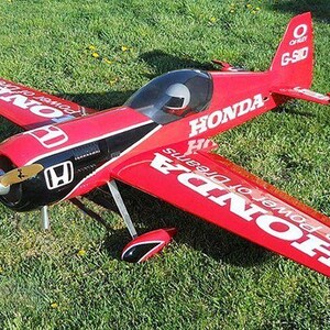 Puede incluir: Un avión rojo, negro y blanco controlado por radio con las palabras "Honda The Power of Dreams" en las alas. El avión tiene una hélice y una pequeña cabina.