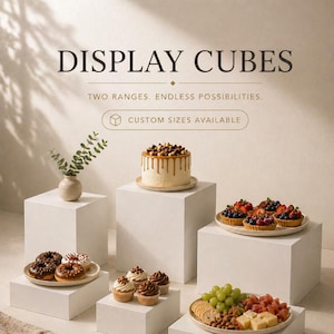 May include: White display cubes presenting an assortment of desserts: a cake with caramel, cupcakes, donuts, and fruit tarts. The image includes the text "DISPLAY CUBES" and "CUSTOM SIZES AVAILABLE".