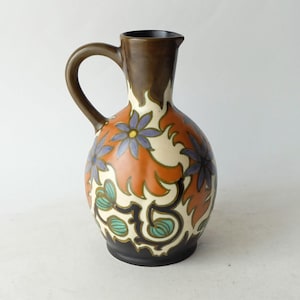 May include: A brown ceramic jug with a floral design in shades of orange, blue, green, and white. The jug has a wide base and a narrow neck with a handle.