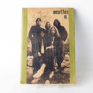 Peut inclure: Un cahier vintage à spirales avec une image sépia des Beatles. La couverture porte le mot "Beatles" et le chiffre "8" en vert et bleu. La tranche est verte.