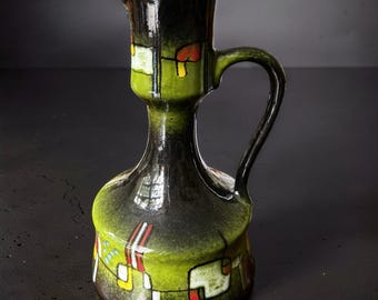 May include: A ceramic pitcher with a glossy finish, featuring a gradient of dark black to vibrant lime green. The body is decorated with abstract geometric patterns in white, red, and yellow, including rectangular shapes and thin black lines.