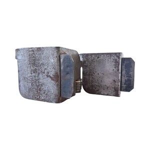 May include: A weathered, antique metal lock with a rectangular body and a hinged door. The lock is a dull gray color with signs of rust and wear, suggesting age and use. The design is simple and functional.