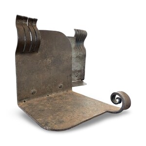 May include: A weathered, L-shaped metal bookend with a rustic, industrial aesthetic. The bookend features a flat base, a vertical support with three curved accents, and a decorative scroll detail. The metal has a dark, aged finish.