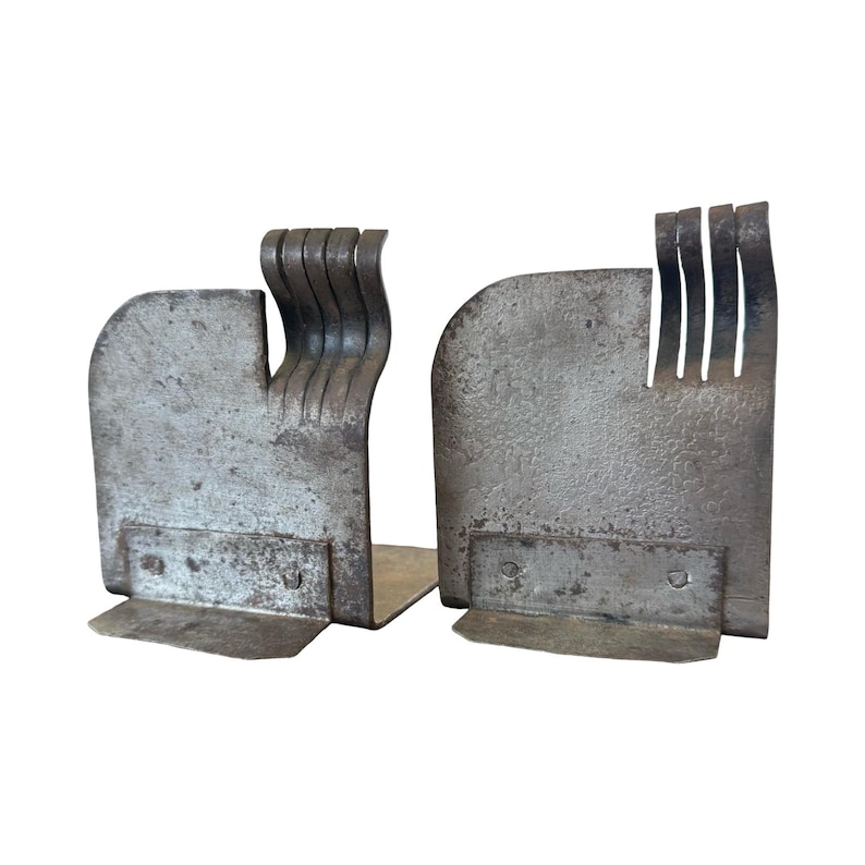 May include: Pair of industrial-style metal bookends. Each bookend has a rectangular base and a curved, textured body. One features a series of vertical, curved metal pieces, while the other has a series of vertical slits.