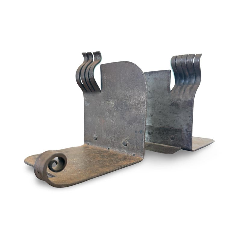May include: A pair of handcrafted metal bookends. The bookends are a dark gray color with a textured finish. Each bookend has a flat base, a vertical support, and a decorative scroll or wave design. The bookends are designed to hold books upright.