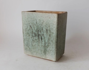 May include: A rectangular ceramic vase with a light green glaze and a speckled finish. The vase has a subtle, organic texture.