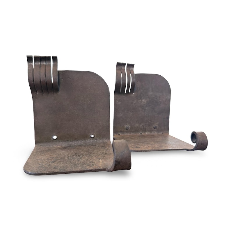 May include: Pair of rustic, dark brown metal bookends. Each bookend has a curved base, a vertical back with decorative cutouts, and a curled end. The metal has a textured, aged appearance.