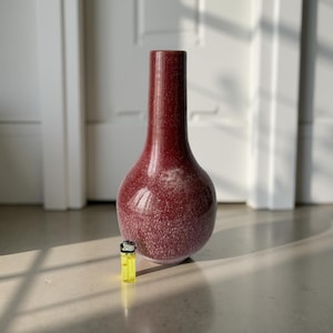 Può includere: Un vaso alto, color amaranto con una texture maculata. Il vaso ha un corpo arrotondato e un collo lungo e sottile. Un accendino giallo è accanto al vaso. Il vaso è probabilmente utilizzato per scopi decorativi. Altezza circa 20 cm.