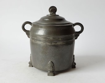 May include: A pewter sugar bowl with a lid and two handles. The bowl has a hammered finish and sits on three feet.