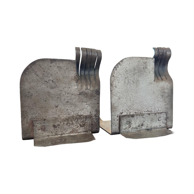 May include: Two weathered, metal bookends. Each bookend has a rectangular base and a curved, upright section with a series of vertical, curved tabs. The metal has a mottled, aged appearance, suggesting use and age. The bookends are designed to hold books upright.