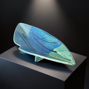 Op de afbeelding: Een blauw en groen keramisch decoratief schaaltje in de vorm van een blad. Het schaaltje heeft een textuur met zwarte penseelstreken en wordt ondersteund door een kleine standaard. Afmetingen in centimeters.