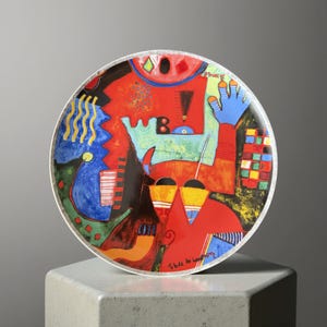 Op de afbeelding: Een decoratieve schaal met een kleurrijk abstract ontwerp. De schaal heeft een witte rand en een levendige mix van rode, blauwe, gele en groene vormen. Het ontwerp bevat een blauwe hand, geometrische patronen en de tekst "Tribute to Kandinsky".