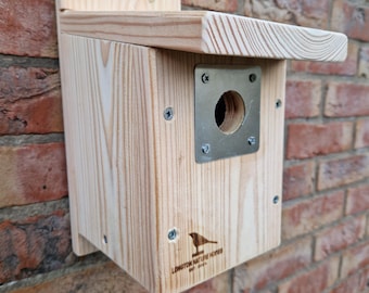Könnte beinhalten: Ein Vogelhaus aus Holz mit einem Metall-Eingangsloch und einem schrägen Dach. Das Vogelhaus ist an einer Backsteinwand montiert und trägt den Schriftzug "Longton Nature Reserve" auf der Vorderseite.