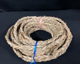 May include: Coiled natural fiber rope, tightly woven and secured with a pink and blue tie. The rope is a light brown color, with a braided texture. The rope is likely used for crafting or decorative purposes.