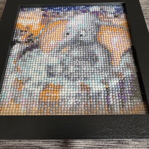 May include: A framed diamond painting with a colorful abstract design featuring shades of blue, purple, orange, and white.
