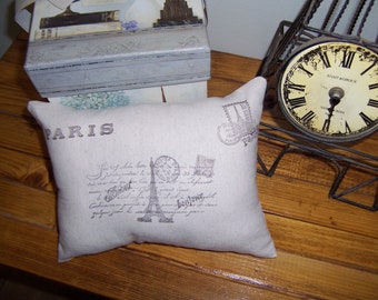 May include: A beige throw pillow with a black and white print of the Eiffel Tower and the word "PARIS" on it. The pillow has a vintage Parisian theme with handwritten text and postage stamps.