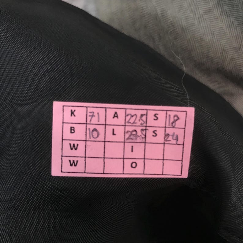 May include: A close-up of a pink tag with black text and measurements. The tag is on a black fabric. The tag has the following measurements: A 22.5, L 29.5, S 18, S 24.