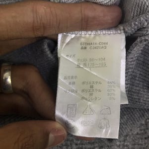 May include: A close-up of a grey sweatshirt label with text. The label includes the product code STDHA14-C044 and size information. The label also lists the fabric composition: 65% polyester, 35% cotton, 62% polyester, 33% cotton, and 5% polyurethane.