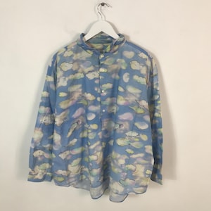 May include: A long-sleeved button-down shirt with a sky blue background and a pattern of white, yellow, and pink clouds. The shirt has a mandarin collar and is hanging from a white hanger.