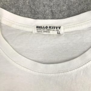 May include: White t-shirt with a Hello Kitty logo on the neck tag. The tag reads "HELLO KITTY &copy;1976, 2021 SANRIO CO., LTD. TOKYO, JAPAN LL".