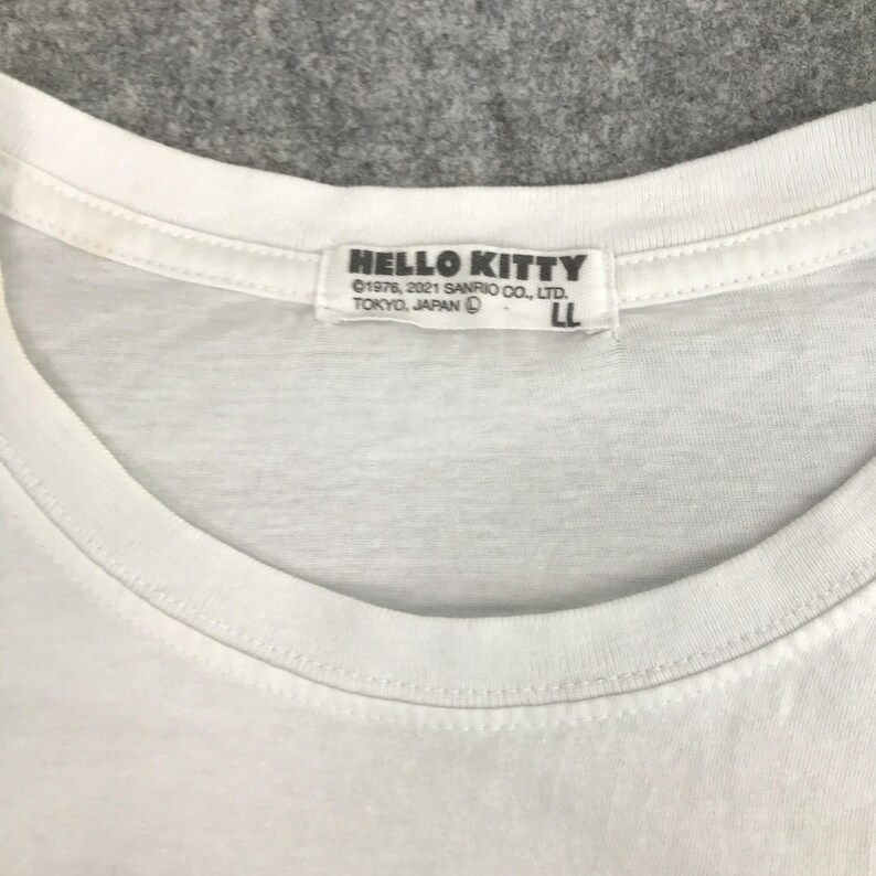 May include: White t-shirt with a Hello Kitty logo on the neck tag. The tag reads "HELLO KITTY &copy;1976, 2021 SANRIO CO., LTD. TOKYO, JAPAN LL".