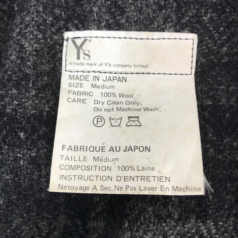 May include: A close-up of a label with text in English and French. The label states "MADE IN JAPAN", "SIZE Medium", "FABRIC 100% Wool", and "CARE Dry Clean Only. Do not Machine Wash."
