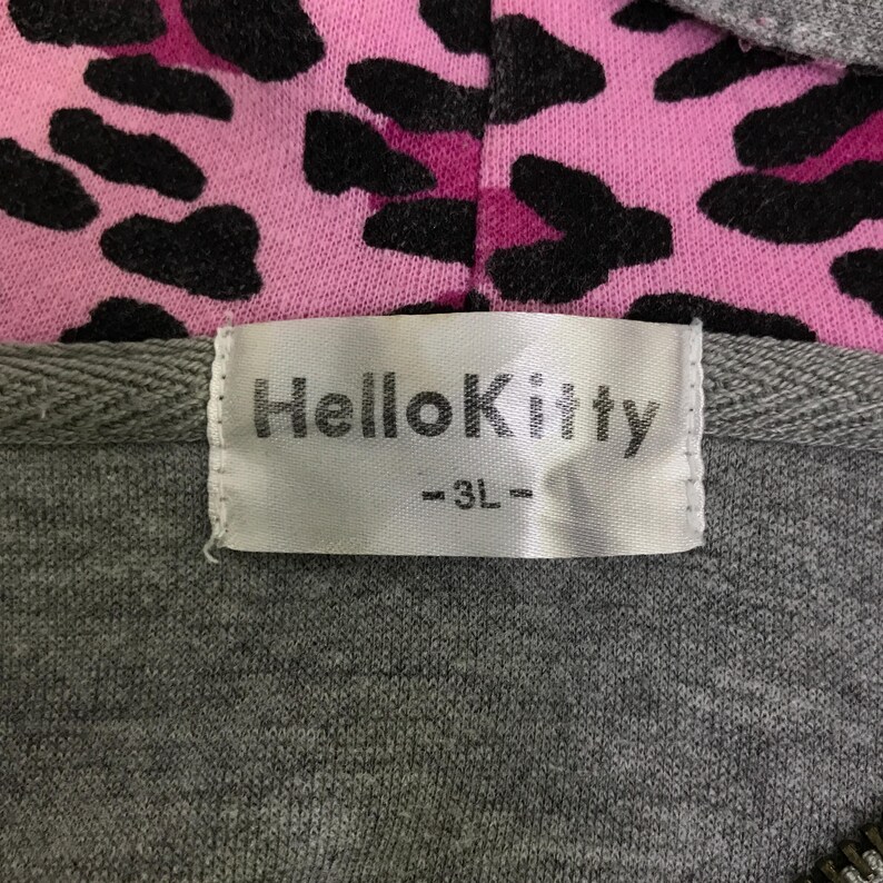 May include: A gray zip-up hoodie with a pink and black leopard print hood lining. The label reads "Hello Kitty -3L-". The hoodie is made of a soft, comfortable material.