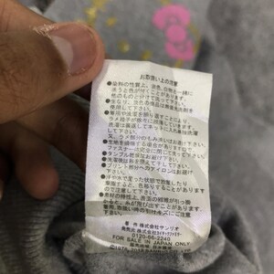May include: Close-up of a gray fabric tag with Japanese text and the words "FOR SALE IN JAPAN ONLY." The tag also includes the Sanrio copyright information. The tag is attached to a gray garment.