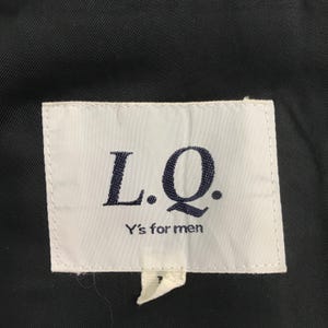May include: A close-up shot of a white label with the text "L.Q." in dark blue, and "Y's for men" below. The label is attached to a dark fabric, possibly a piece of clothing.