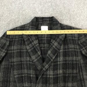 May include: A grey and black plaid blazer with a notched collar. A wooden ruler is placed across the blazer, measuring its width. The blazer has a herringbone pattern and a tag with the letter "Y".