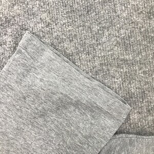 Pu&ograve; includere: Primo piano di un tessuto grigio, possibilmente una manica o un orlo di un capo. Il tessuto ha un aspetto strutturato, con dettagli visibili di maglia o tessitura. Il bordo &egrave; ripiegato e cucito.