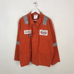 May include: Orange work coverall with reflective stripes on the shoulders and sleeves. Features the ExxonMobil and Esso logos on the chest. Includes two chest pockets and a button-down front.