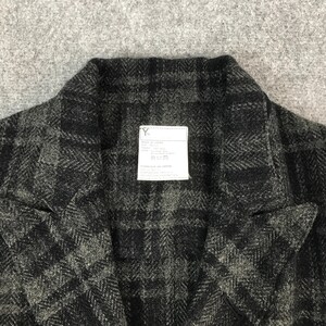 May include: A close-up shot of a dark grey and black checked jacket. The jacket features a notched collar and a small white label with text. The fabric has a textured finish.