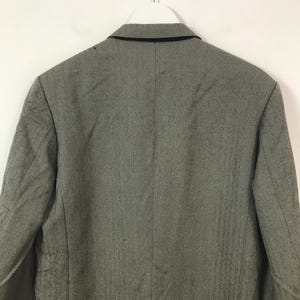 May include: A grey blazer with a black collar, suspended from a white hanger. The rear view of the blazer reveals its tailored design and fabric texture. The blazer has a classic, professional style.