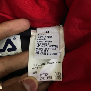 May include: Close-up of a garment tag with the brand logo and text. The tag is white with black text, listing the shell, lining, and padding materials as 100% nylon and 100% polyester. The tag also includes the size, RN number, and country of origin.