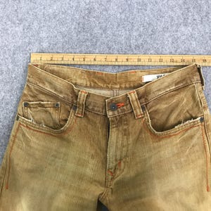 May include: A pair of brown denim jeans with orange stitching. The jeans have a faded look and a worn-in appearance.