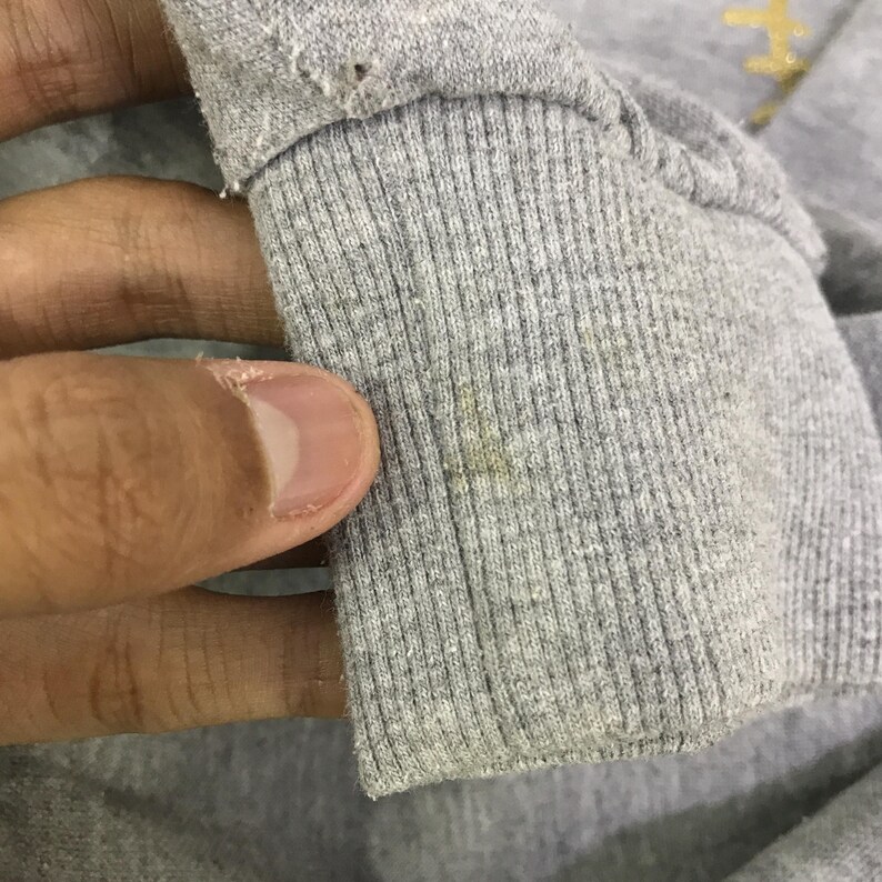 May include: Close-up of a gray sweatshirt cuff with ribbed detailing. The cuff shows signs of wear, including small holes and discoloration. The fabric appears to be a soft, knit material.