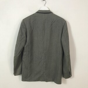 May include: A grey blazer with a subtle vertical stripe pattern, hanging on a white hanger. The back of the jacket is visible, showing the collar and buttoned cuffs. The blazer is made of a textured fabric.